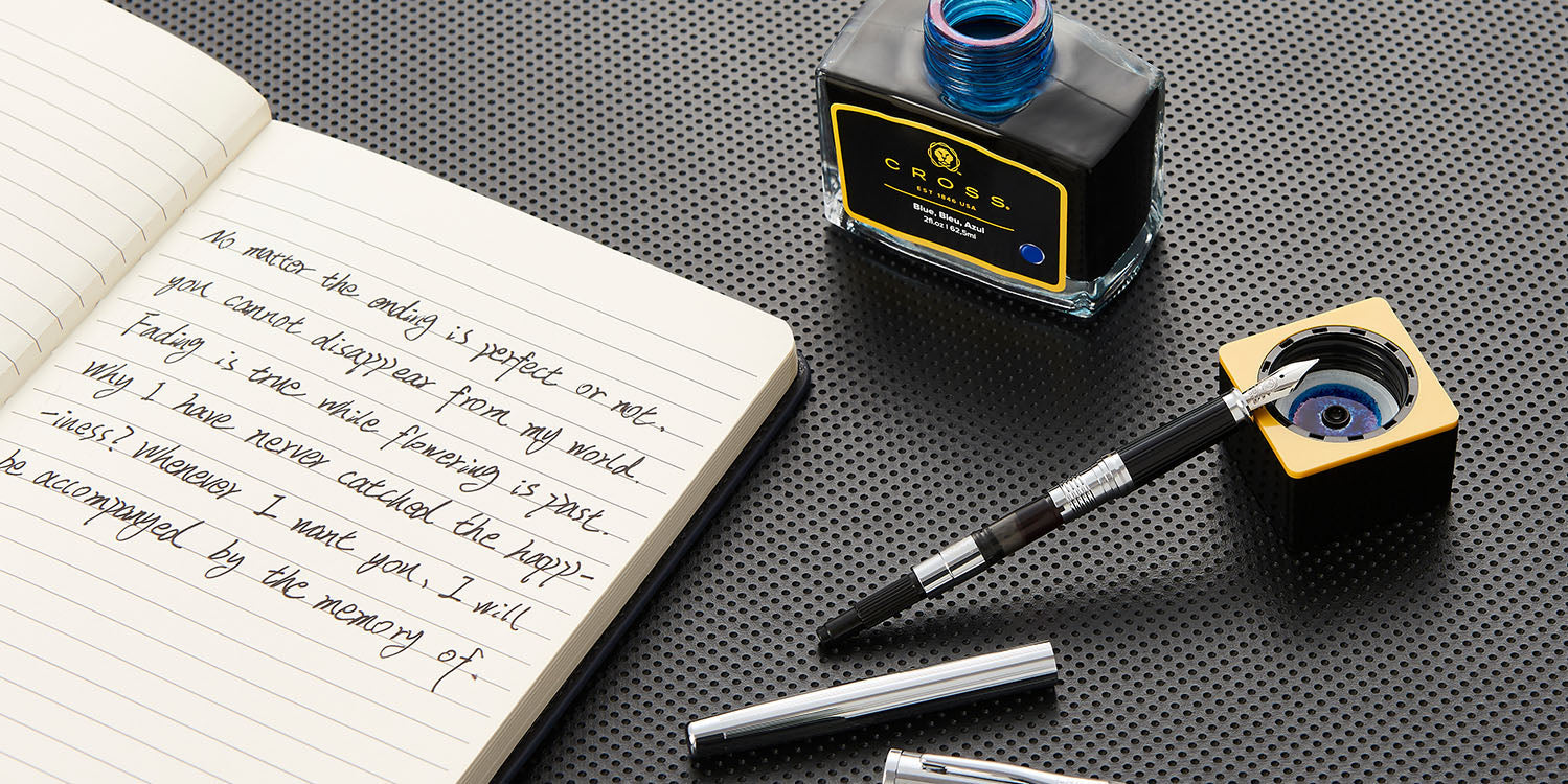 Bottle of Cross blue fountain pen ink next to a disassembled Century II Chrome Fountain Pen, revealing its ink converter.